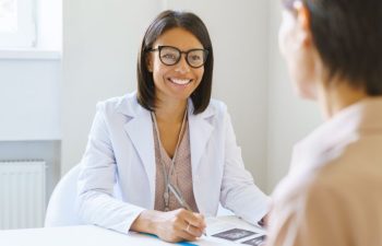 Smiling friendly african american woman doctor in white medical uniform discussing ultrasound results with female patient