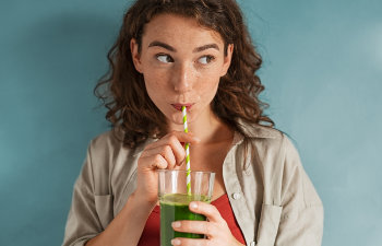 girl with curly brown hair drinks through a straw green smoothie