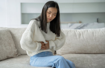 woman in a white blouse is sitting on the couch and feels a strong abdominal pain